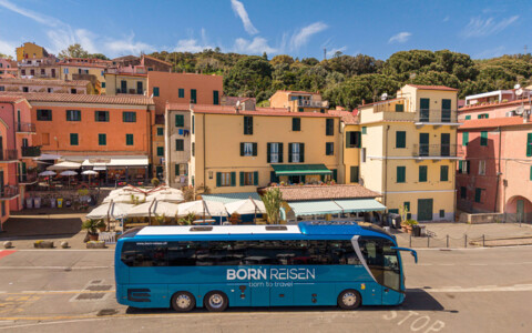 Born Reisen Komfortcar vor farbenfrohen Häusern eines mediterranen Küstenortes direkt am Hafen.