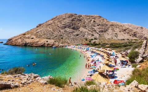 Beliebter Kiesstrand auf der Insel Krk in Kroatien mit Sonnenschirmen und Badegästen.