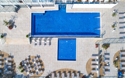 Aussenpool im Hotel Malin mit Blick aufs Meer, umgeben von Liegestühlen und Palmen.