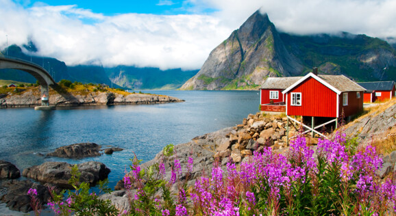 Traditionelles rotes Fischerhaus am Fjord mit Blick auf Berge und Brücke in Norwegen – Nordkap Reise