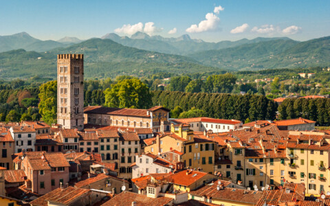 Blick über die Dächer von Lucca mit Kirchturm und den Hügeln der Toskana im Hintergrund.