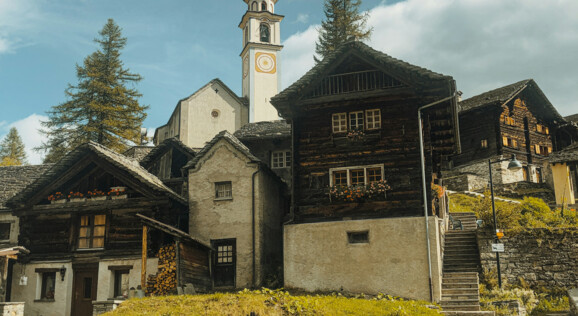 Das Dorf Bosco Gurin liegt idyllisch in einem tiefen Tal umgeben von majestätischen Schweizer Alpen. Die traditionellen Holzhäuser mit ihren charakteristischen Steindächern fügen sich harmonisch in die natürliche Umgebung ein. 