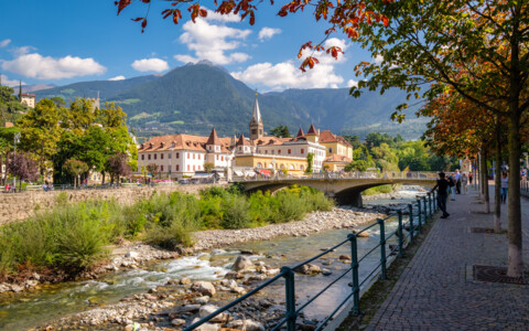 Spazierpromenade entlang der Passer in Meran mit historischen Gebäuden und Südtiroler Bergkulisse.