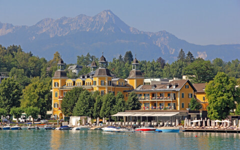 Blick vom Wörthersee auf das bekannte Schlosshotel Velden und die umliegende Berglandschaft.