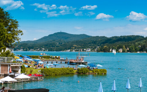 Wörthersee mit Ausflugsschiffen und Segelbooten vor der grünen Kärntner Berglandschaft.
